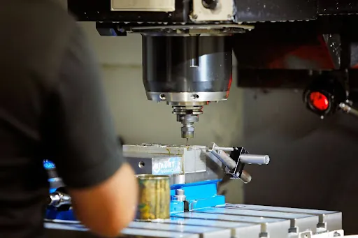 A person operates a CNC milling machine, focusing on precision parts for aerospace and medical manufacturing.